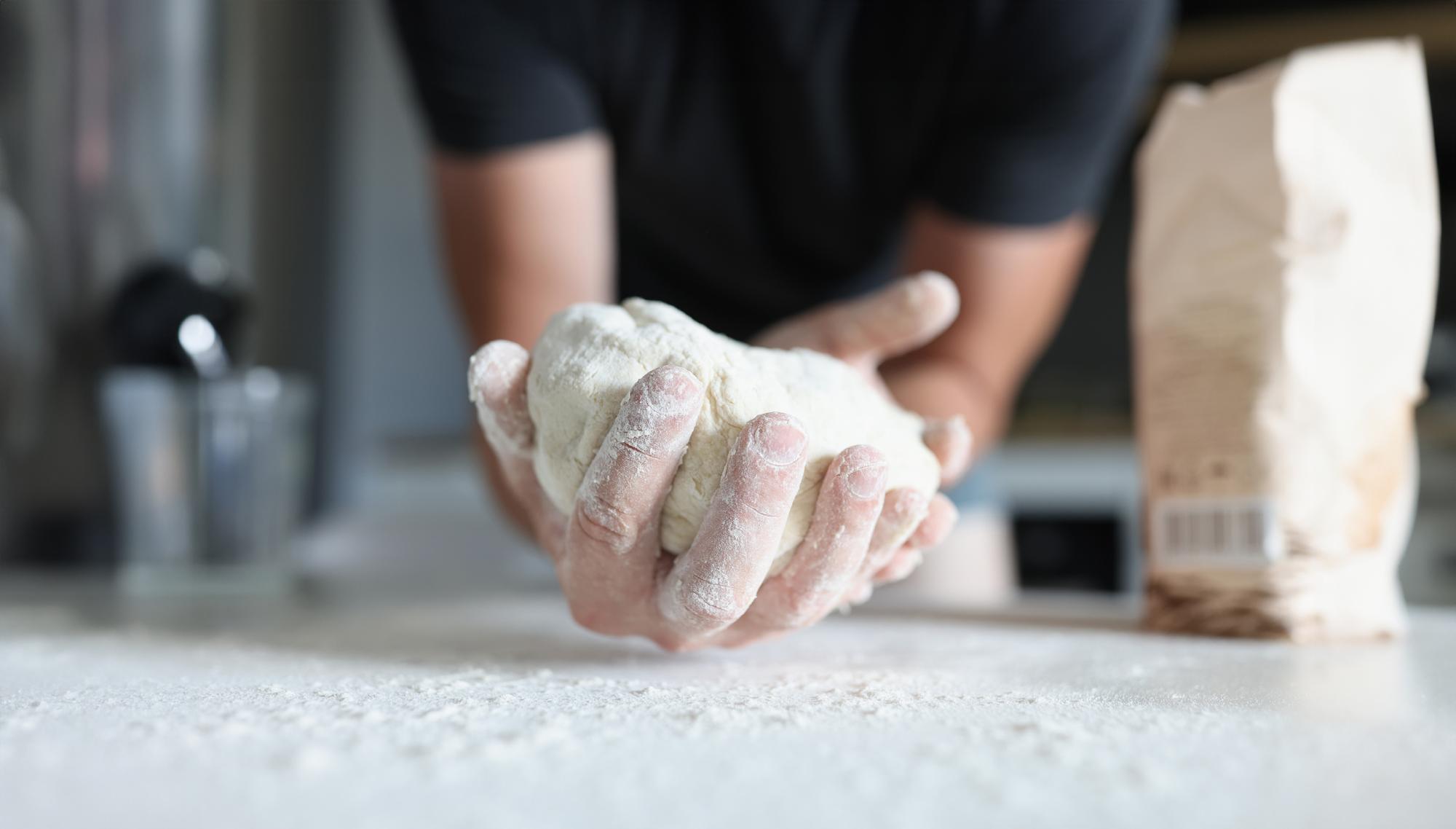 Hands kneading dough on floured surface